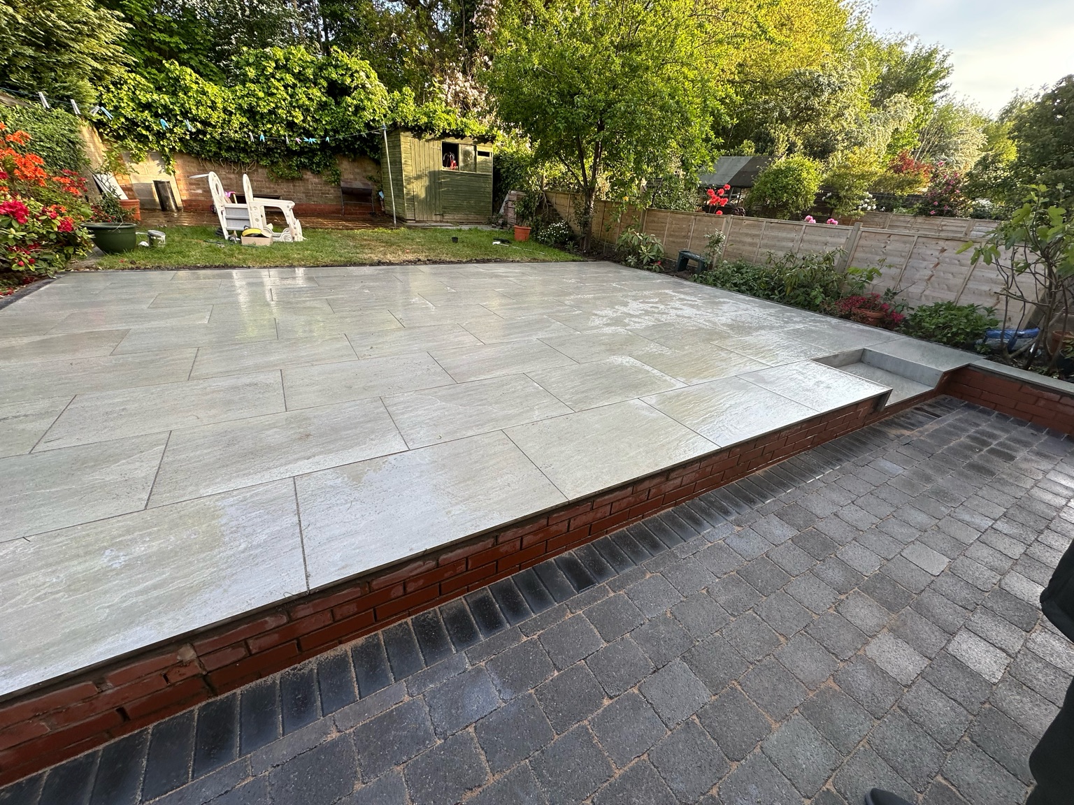 Wider view of a raised porcelain patio with block paving in the foreground