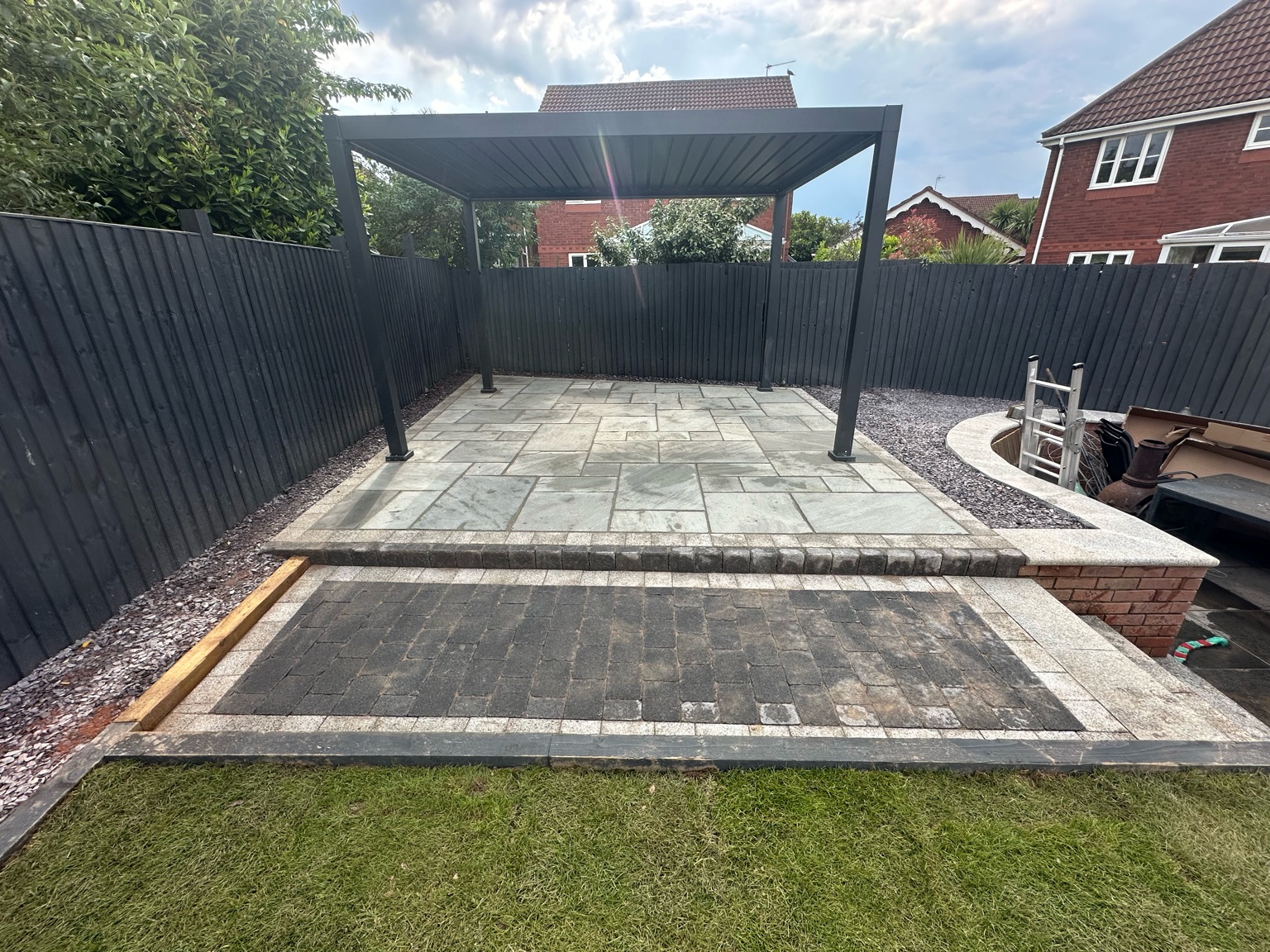 Sandstone patio under a dark grey aluminium pergola with black fencing, Worcester